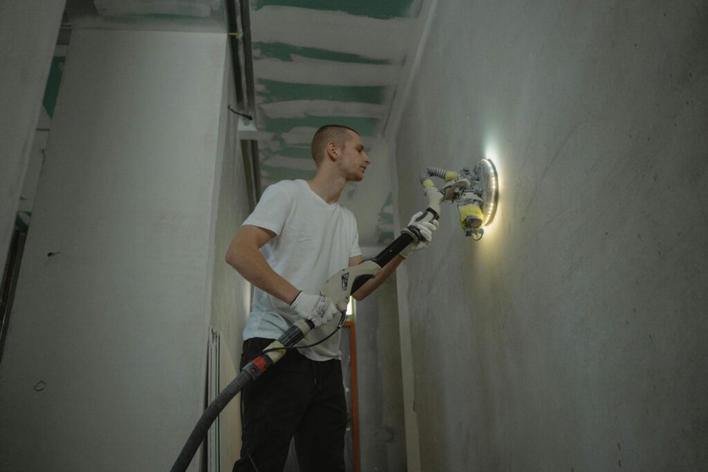 pexels photo 6473965 6473965 A man sanding an interior wall with an automatic sanding tool during renovation work indoors.
